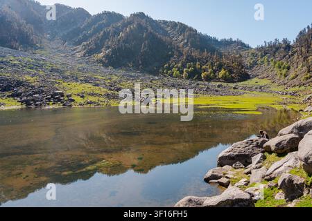 Ein ruhiger Alpensee, eingebettet zwischen felsigen Berghängen und üppigen grünen Wiesen im Himalaya. Stockfoto