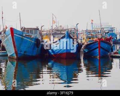 Bunte blaue Holzfischerboote, die in einem belebten Hafen in Da Nang, Vietnam, vor Anker liegen, mit Reflexionen im ruhigen Wasser. Stockfoto