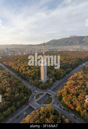 Luftbild des Sofia-Fernsehturms, umgeben von einem lebendigen Herbstwald, mit einer Straßenkreuzung und einem Tunnel im Vordergrund und der Stadt Skyline in Sofi Stockfoto