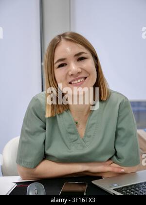 Nahaufnahme-Porträt einer freundlichen jungen Ärztin oder Neurologin in grüner OP-Bekleidung, die am Arbeitsplatz in einem modernen Krankenhaus in die Kamera lächelt Stockfoto