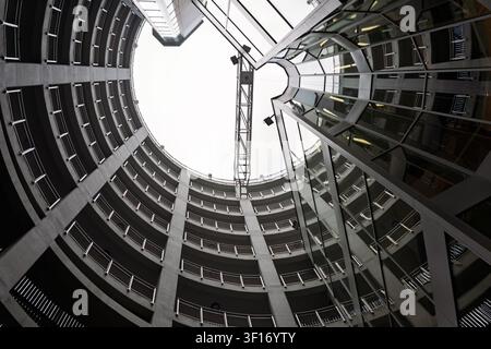 Niedriger Fischaugenblick auf ein modernes kreisförmiges Gebäudeatrium mit geschwungenen Betonbalkonen und einer reflektierenden Glasfassade Stockfoto