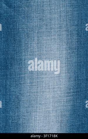 Nahaufnahme von klassischem Jeansstoff in Blau. Der detaillierte Stoff zeigt eine diagonale Webart und eine verblasste Textur. Die Indigo-Farbe hat einen helleren abgenutzten Bereich in der Mitte. Per Stockfoto