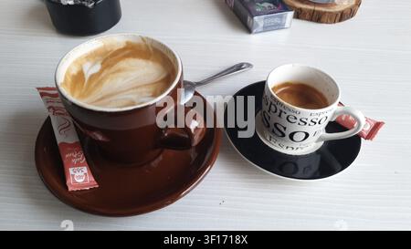 Frisch zubereiteter Cappuccino und Espresso nebeneinander auf einem Café-Tisch serviert, der zwei klassische italienische Kaffee-Favoriten in einem gemütlichen Café zeigt Stockfoto