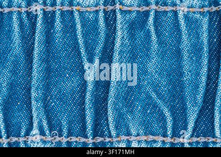 Detaillierte Makroaufnahme von blauem Denimtextil, das ein diagonales Twillgewebe, weiße Nähte und die Textur des Stoffes zeigt. Natürliches Licht hebt die Faserdetails hervor. Stockfoto