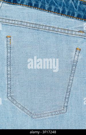 Hellblauer Denimstoff, Nahaufnahme zeigt die Gesäßtasche mit kontrastierenden orangefarbenen Nähten. Strukturierte Webart, klare Linien heben das lässige Modedetail hervor Stockfoto