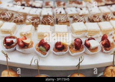 Zarte Backwaren säumen ein weißes Tablett. Süße Leckereien enthalten Erdbeeren und Sahne. Mit Obst gekrönte Desserts glänzen im sanften Licht. Jeder Bissen verspricht Stockfoto