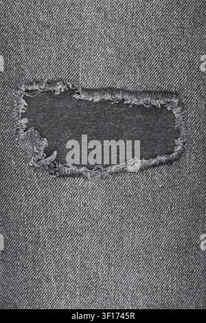 Nahaufnahme von altem, abgenutztem grauem Denim. Zerrissenes rechteckiges Loch mit ausgefransten Rändern zeigt die Stofftextur. Hintergrund für Design, Mode oder Konzepte der Langlebigkeit Stockfoto