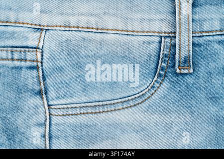Detaillierte Makroaufnahme von hell gewaschenem Denimstoff. Nahaufnahme der vorderen Tasche, des Gürtelschlitzes und der orangefarbenen Nähte an klassischen blauen Jeans. Verblasster Textilhintergrund Stockfoto