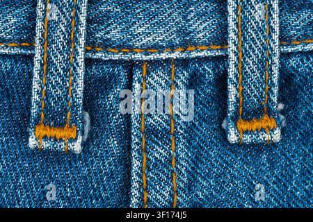 Extremer Nahaufnahm makro von klassischem blauem Denimstoff. Details der gelb-orangen Nähte an den Säumen und Gürtelschlaufen erzeugen eine starke Textur und Hintergrund Stockfoto