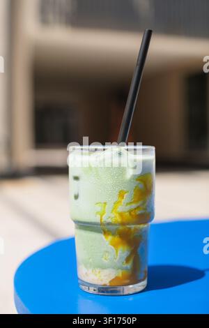 Nahaufnahme eines eisgekühlten Matcha-Mango-Lattes mit Eiswürfeln in einem hohen Glas auf einem Tisch Stockfoto
