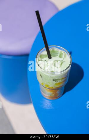 Ansicht von oben eines eisgekühlten Matcha-Mango-Lattes mit Eiswürfeln in einem hohen Glas auf einem Tisch Stockfoto