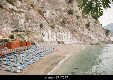 Leere Sonnenliegen und Sonnenschirme am Strand Spiaggia del Lannio bei Sonnenaufgang, Cetara, Salerno, Italien Stockfoto