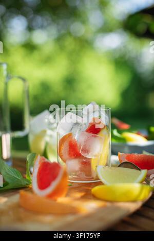Nahaufnahme eines Glases gefüllt mit Eiswürfeln und frischen Grapefruitscheiben auf einem sonnigen Gartentisch Stockfoto