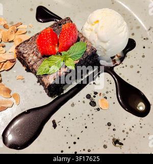 Nahaufnahme eines Schokoladen-Brownies, Vanilleeis, Schokoladensoße, Mandeln, Minzblätter und einer Erdbeergarnitur Stockfoto