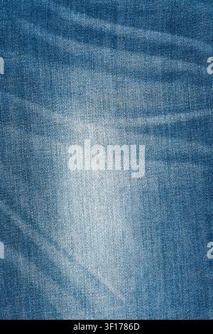 Nahaufnahme-Hintergrund aus klassischem blauem Denimstoff. Das Material ist zerknittert und verrunzelt mit einem verblassten, abgenutzten Fleck in der Mitte. Die detaillierte Textur zeigt diagonale Twi Stockfoto