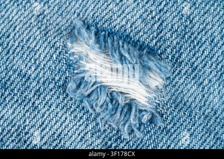 Detaillierte Makroaufnahme von abgenutztem blauem Denim mit sichtbarer Gewebestruktur, ausgefranster Rippe, die weiße Innengarnfäden freilegt. Weiches natürliches Licht hebt den Stoff hervor Stockfoto