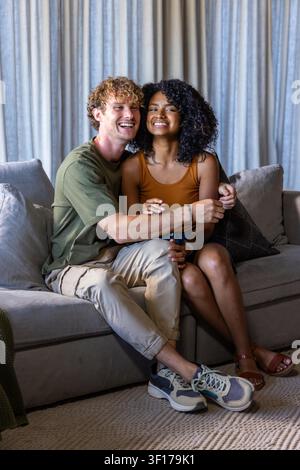 Verschiedene Paare sitzen eng auf einem hellgrauen Sofa im Wohnzimmer mit gemustertem Kissen. Sitzend, intim, gemütlich, Zuhause, Kissen, Teppich, Vorhang Stockfoto