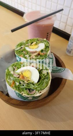 Frischer Salatm wrap serviert mit einem gemischten Beeren-Fruchtsmoothie, der ein gesundes und nahrhaftes Frühstück oder ein leichtes Mittagessen in einem modernen Café bietet. Stockfoto