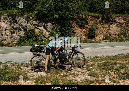 Bikepacking-Fahrer macht eine kurze Pause neben einem voll beladenen Tourenrad auf einer Bergstraße in Montenegro. Abenteuerradfahren und Langstrecke Stockfoto