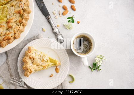 Oberblick auf ein köstliches Stück hausgemachte Rhabarber-Tarte mit Mandelstiften auf einem Teller, serviert mit einer Tasse schwarzem Kaffee, einem Vintage-Messer und frischer Blume Stockfoto