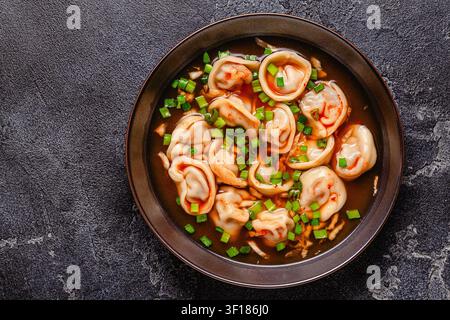 Mandu-Teigtaschen-Suppe. Teigtaschen werden in einer Schüssel mit Brühe und grünen Zwiebeln serviert, Blick von oben. Stockfoto