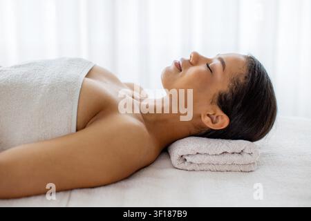 Junge schwarze Frau mit geschlossenen Augen entspannt auf dem Spa-Tisch Stockfoto