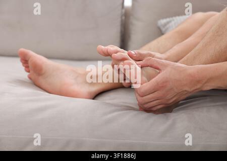 Mann massiert seinen Fuß auf dem Sofa zu Hause, Nahaufnahme Stockfoto
