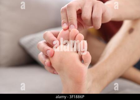 Mann massiert seinen Fuß auf dem Sofa zu Hause, Nahaufnahme. Platz für Text Stockfoto