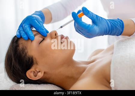 Seitenansicht einer jungen schwarzen Frau, die eine kosmetische Füllstoffinjektion in der Nähe der Nase erhält Stockfoto