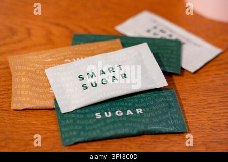 Einzelne Papiersüßstofftüten, einschließlich der Marken „Smart Sugar“ und „Brown Sugar“, ordentlich über eine warme Holzoberfläche verteilt in einem Mo Stockfoto