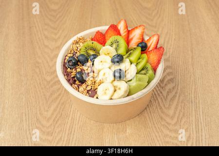 Gesunde Acai-Smoothie-Schale mit frischen Erdbeeren, Kiwi, Bananenscheiben, Blaubeeren und knuspriger Granola in einem Pappbecher Stockfoto