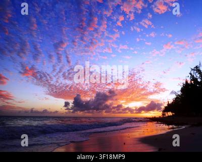 Lebendiger Sonnenuntergang über einem tropischen Strand mit farbenfrohen Wolken und Meereswellen Stockfoto
