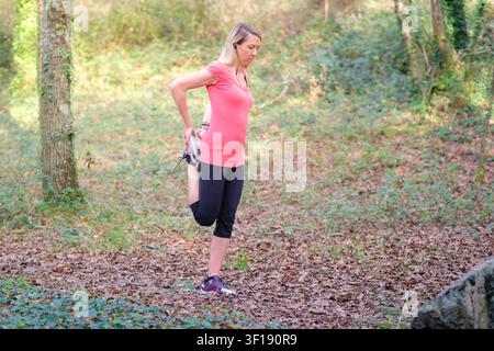 Frau, die sich aufwärmt und Beinstreckung in natürlicher Außenumgebung macht Stockfoto