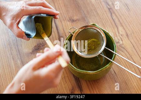 Matcha-Pulver in eine Schüssel sieben für ein selbstgemachtes Eislatterezept Stockfoto