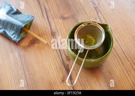 Matcha-Pulver in eine Schüssel sieben für ein selbstgemachtes Eislatterezept Stockfoto