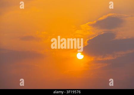 Goldener Sonnenuntergang mit teilweise hinter Wolken versteckter Sonne in einem orangefarbenen Himmel Stockfoto