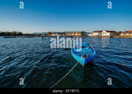 Blaues Fischerboot, das in der Missolonghi-Lagune vor Anker liegt, mit traditionellen Pfahlhäusern und Holzstegen im Hintergrund. Ein friedlicher mediterraner Fischfang Stockfoto