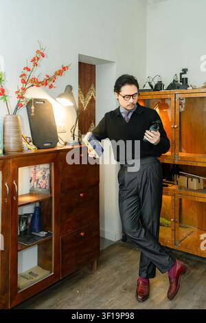 Eleganter asiatischer Mann in einem schicken lässigen schwarzen Rollkragenpullover und einer Brille, posiert in einem luxuriösen Vintage-Arbeitszimmer, anspruchsvolles männliches Model-Fotopapier Stockfoto