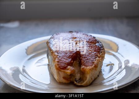 Nahaufnahme eines gebratenen Lachsfilets mit knuspriger goldener Haut, serviert auf einem weißen Keramikteller Stockfoto