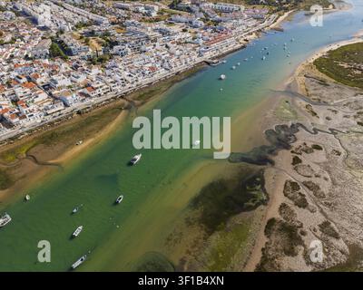 Luftbild der Küstenstadt Cabanas mit weißen Gebäuden, kleinen Booten, die im türkisfarbenen Kanal festgemacht sind, und sandigen Ufern in Cabanas, Faro, Portugal Stockfoto