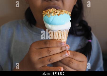 Ein Kind genießt eine Eisdose mit einer blauen Kugel und Nüssen oben drauf Stockfoto