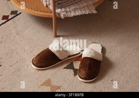 Paar gemütliche braune Wildlederpantoffeln mit weißem Kunstfellfutter auf einem gemusterten Teppich, Komfort und Entspannung zu Hause, das bequeme Schuhwerk deutet auf Erholung hin Stockfoto