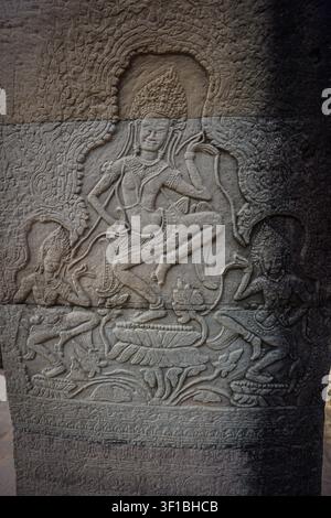 Eine detaillierte Basrelief-Skulptur aus grauem Sandstein zeigt eine zentrale Apsara-Tänzerin mit zwei kleineren Begleiterinnen darunter, flankiert von wirbelnden Blattmusterornamenten. Th Stockfoto