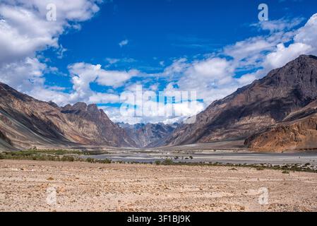 Ein weites Panorama des Nubra-Tals zeigt ein halb-trockenes Flussbett, das von aufragenden felsigen Gebirgszügen eingeschlossen ist. Das aride Gelände im Vordergrund kontrastiert Stockfoto