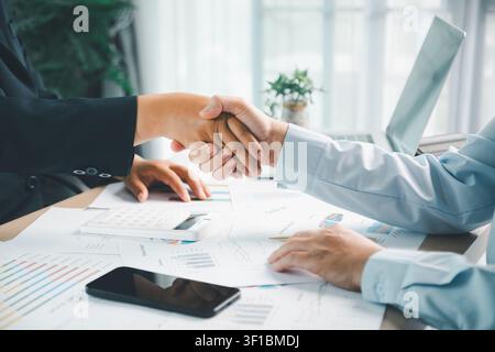 Geschäftspartner, die sich über Finanzdokumenten nach einem erfolgreichen Treffen die Hände schütteln, was Vereinbarung, Partnerschaft, Vertrauen, Verhandlung und Unternehmen darstellt Stockfoto
