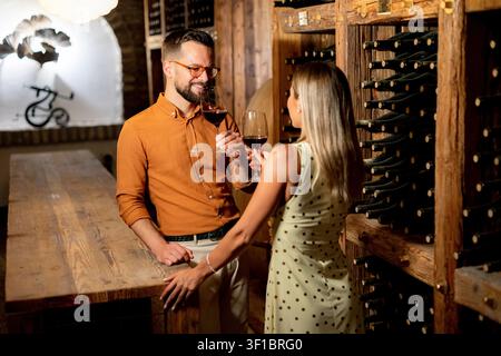 Ein Paar genießt einen entzückenden Moment in einem charmanten Weinkeller und feiert mit Gläsern Rotwein. Die warme Atmosphäre vertieft ihre Verbindung. Stockfoto