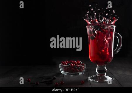 Hellroter Glühwein mit Beeren und Spritzer in einem Weinglas auf schwarzem Holztisch in dunkler Innenraum, Kopierraum. - Fotomontage Stockfoto