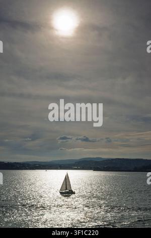 Ein Segelboot segelt im Sonnenreflex vor der Küste von A Coruña, Galicien, Spanien. Stockfoto