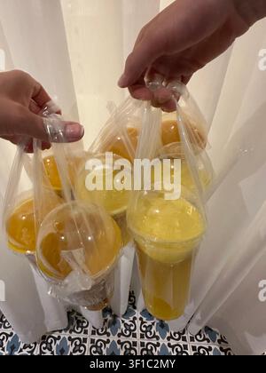 Hände, die mehrere To-go-Becher mit frischem Orangen- und Mangosaft in Plastiktüten halten. Eine Hochwinkelschuss von Menschen, die mehrere Plastikbecher tragen, gefüllt Stockfoto