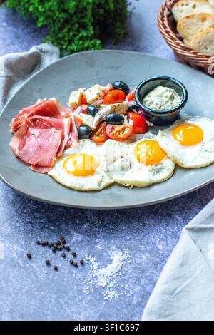 Mediterranes Frühstück mit gebratenen Eiern, Prosciutto, gegrilltem Gemüse und Kräuterdip, serviert auf einem Keramikteller Stockfoto